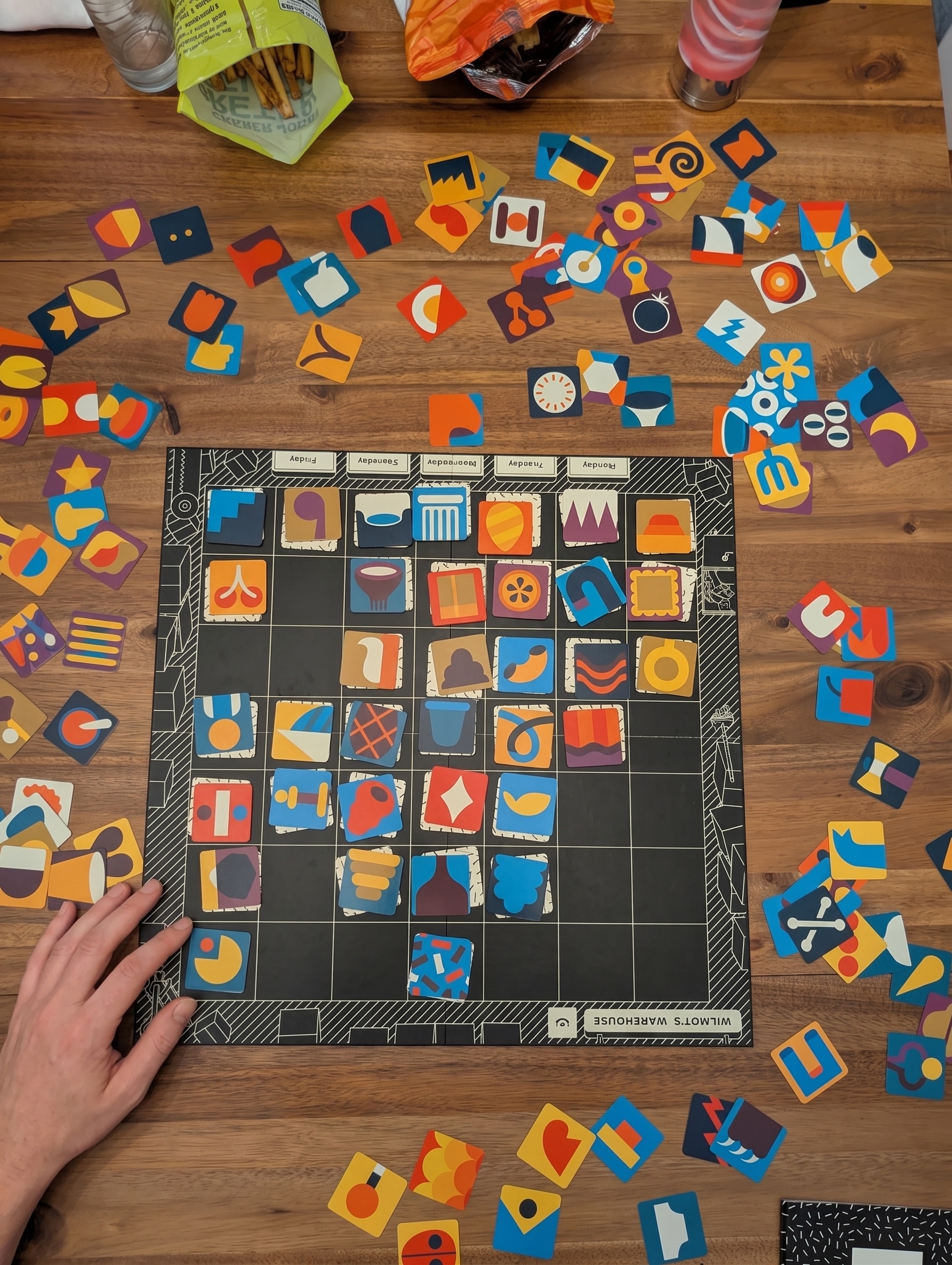 Overhead view of the warehouse board on a wooden table, with a hand placing a product tile
